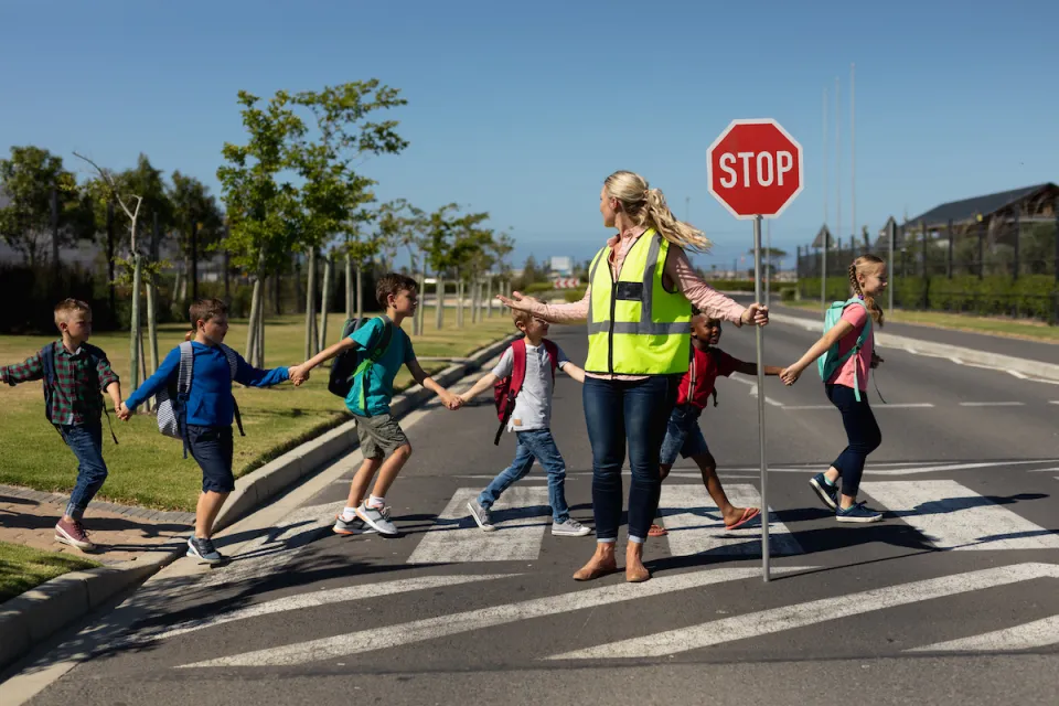 Group of children crossing a street with a crossing guard holding up red Stop sign.